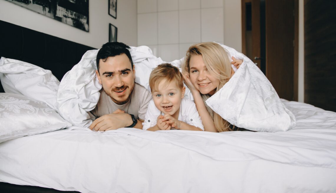 happy-family-lying-under-white-blanket-on-bed-2026-09-21-06-04-23-utc